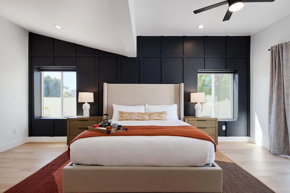 A tranquil bedroom with a plush bed adorned with decorative pillows, nightstands topped with lamps, and expansive windows that let in natural light. The mood is serene and restful, ideal for a peaceful night's sleep or a quiet morning.