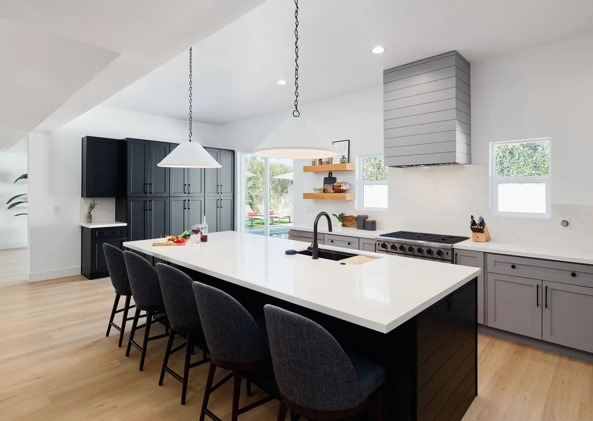 A spacious, light-filled kitchen with a large central island, sleek black cabinetry, and modern appliances. The area is clearly designed for both functionality and gathering, with space for cooking, dining, and entertaining guests. Natural light pours in through generously sized windows, creating an inviting atmosphere.
