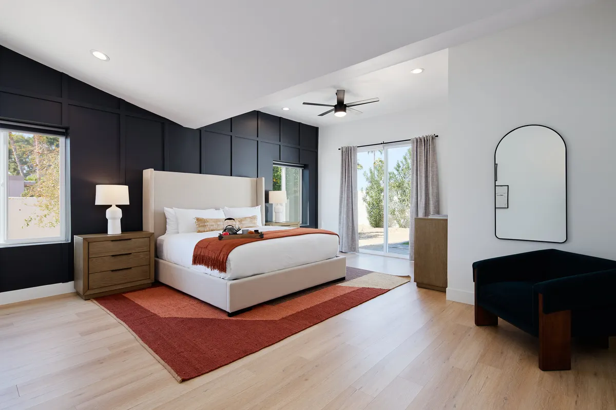 This image showcases a large bed set against a striking black accent wall, bathed in natural light from windows. A ceiling fan and a plush rug add to the serene, modern atmosphere, making it an ideal representation of a primary suite or luxurious bedroom retreat.