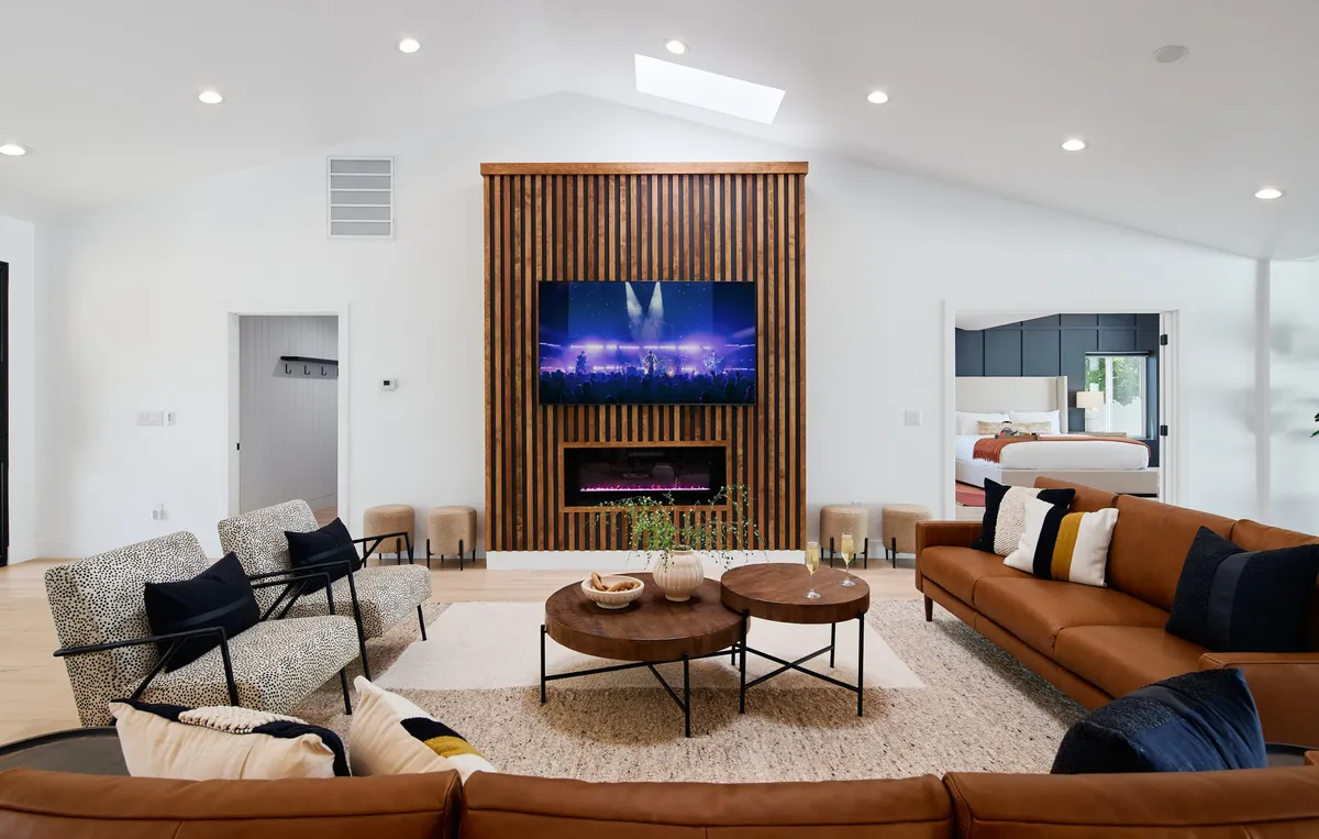 A cozy living room featuring a large television on a wooden accent wall, a coffee table with decorative items, and comfortable seating perfect for family relaxation or movie nights. The space feels both stylish and inviting, suited for intimate gatherings or unwinding after a day out.